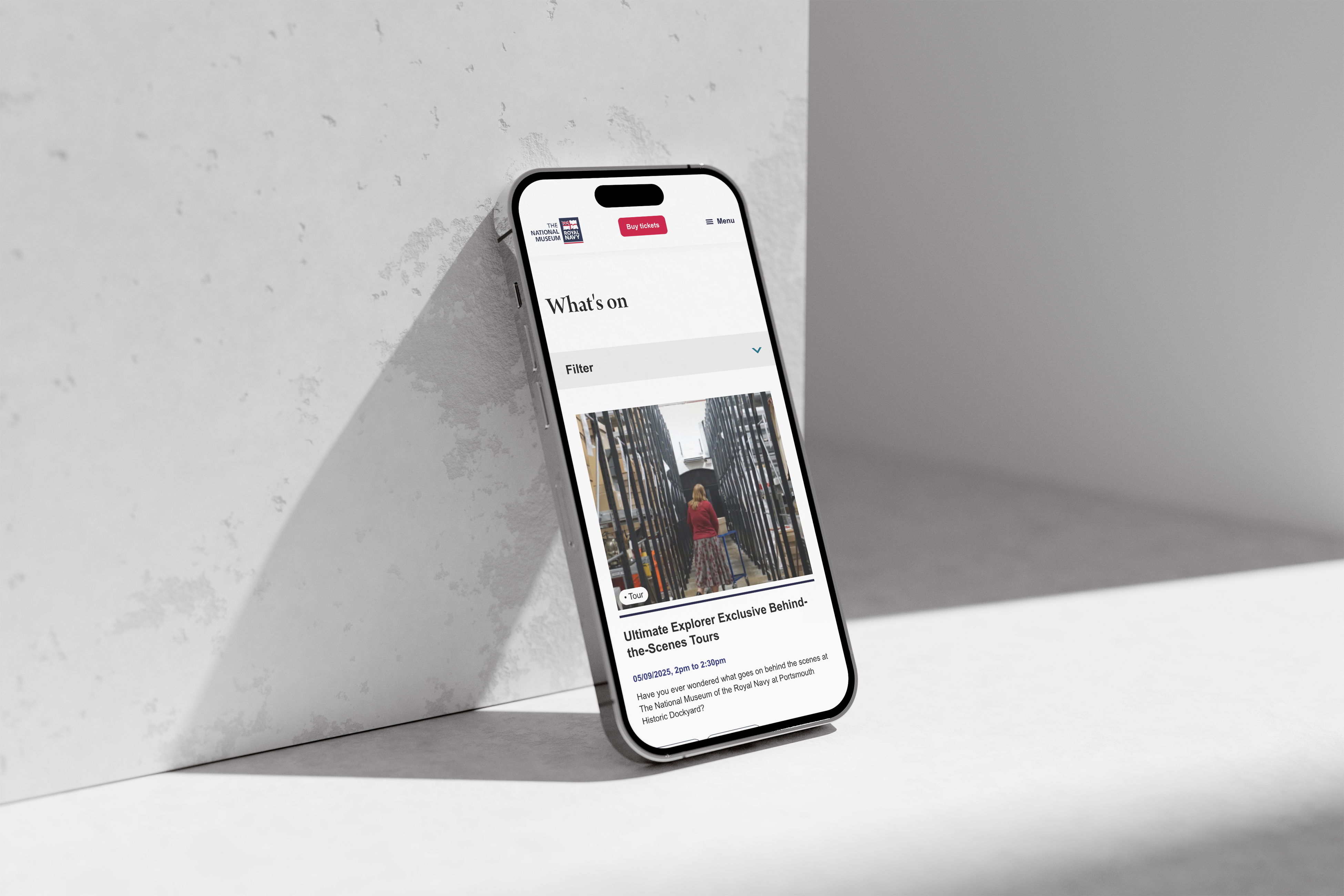 iPhone upright against a concrete block with the NMRN what's on page on screen