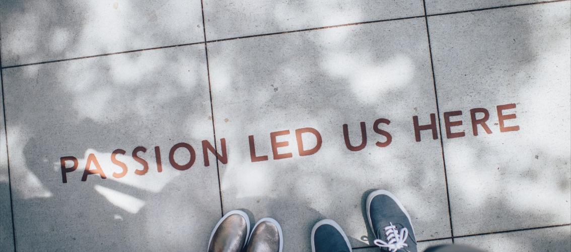 Picture of two people photographed from above. On the ground we can read "Passion led us here".