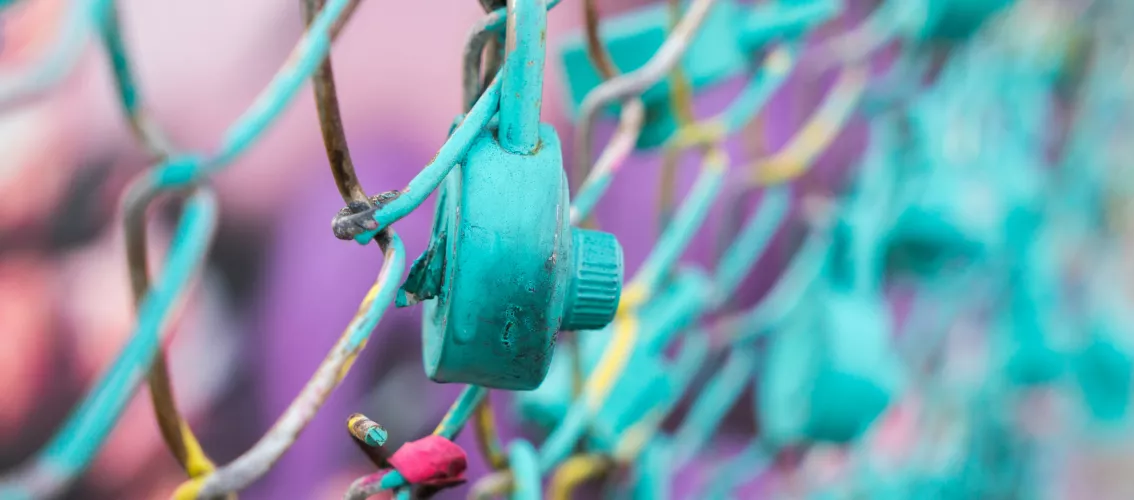 Close-up of a turquoise padlock on a wire fence