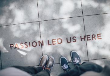 Picture of two people photographed from above. On the ground we can read "Passion led us here".