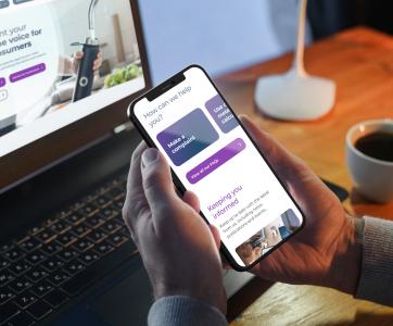 Man holding mobile phone with CCW website on screen, with a laptop in the background showing the CCW homepage