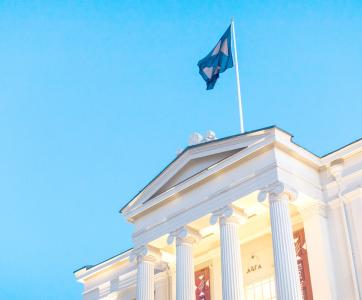 Classical white building with tall columns and a triangular pediment, with a clear blue sky as a background