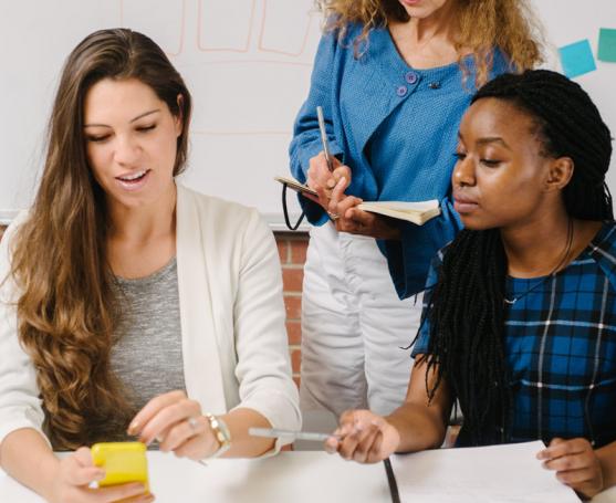 ThreeThree women in a meeting, one showing a phone while others take notes